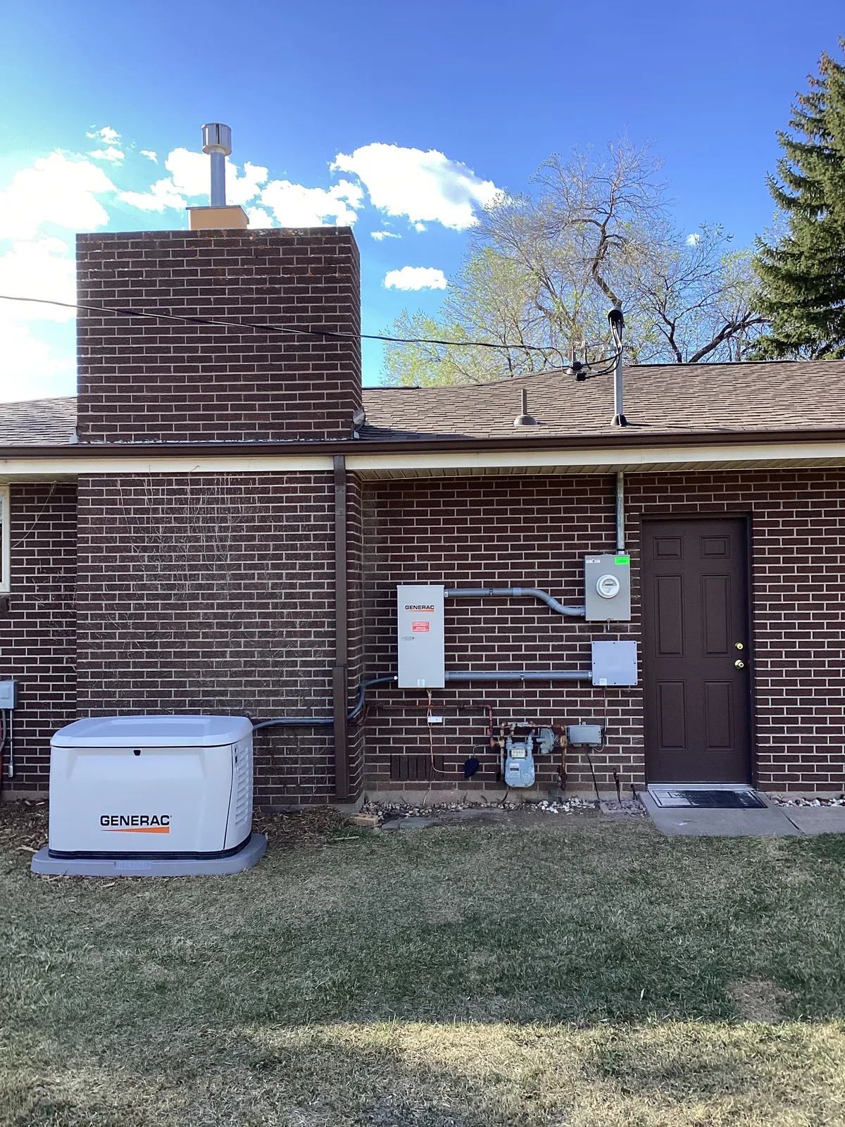 Home standby generator installed beside a brick house, Northern Colorado